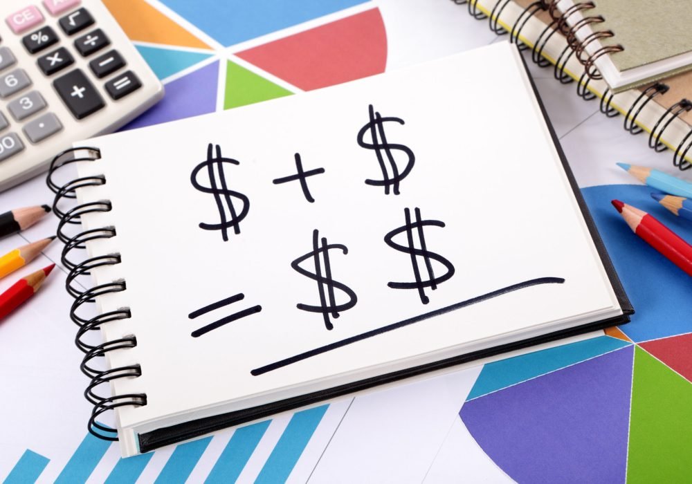 Simple savings or retirement formula written on a notepad surrounded by charts, graphs, calculator, books and pencils.